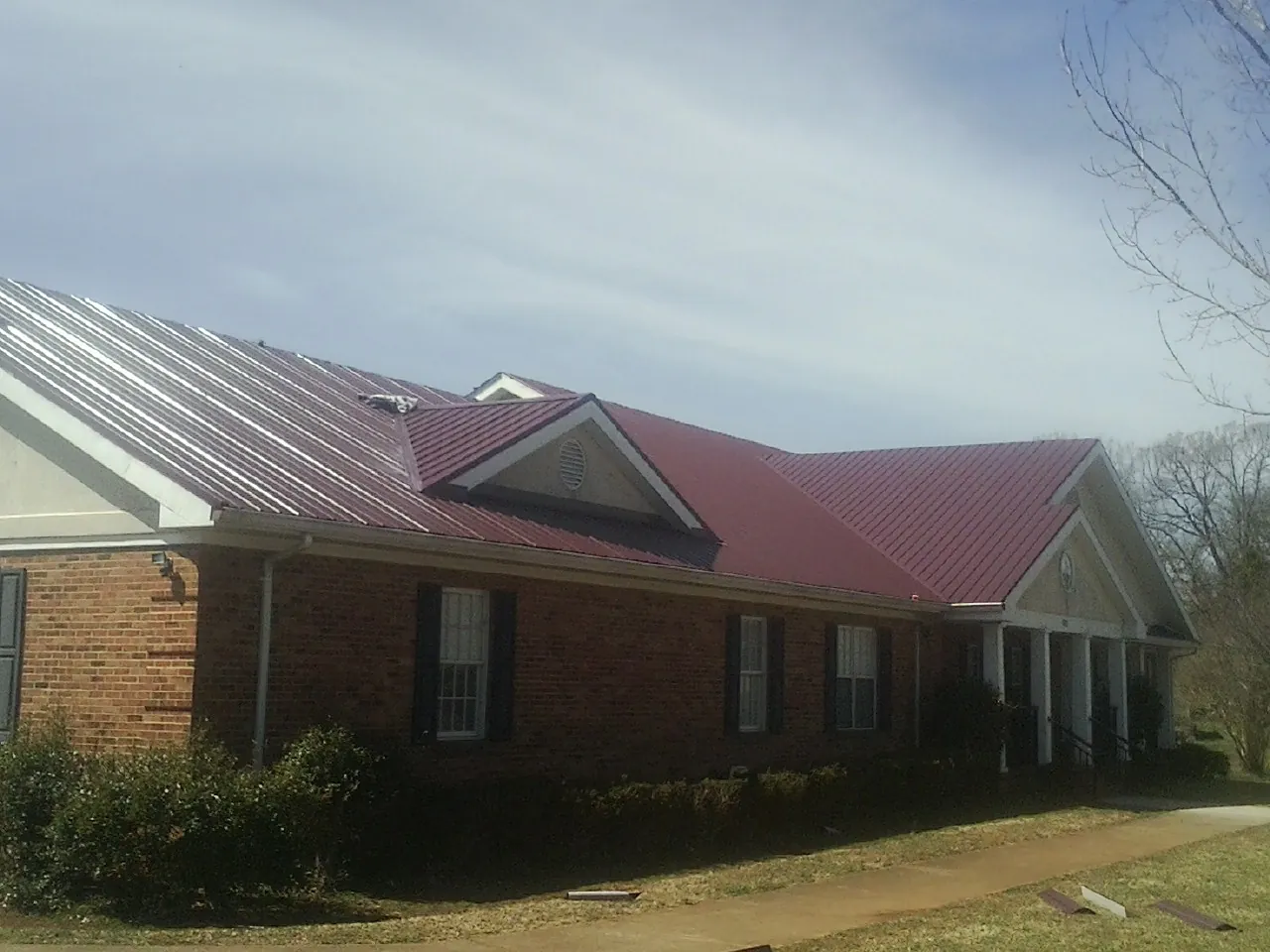 Red metal roof with gabled entries on a long brick building, from a Hail Damage Roof Repair job in Floral Park
