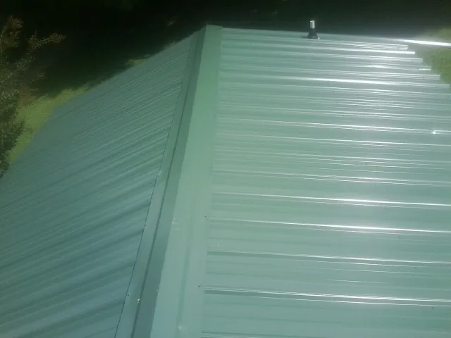 New green metal panels meeting at the ridge of a roof — Flat Roof Repair work by our crew in Floral Park