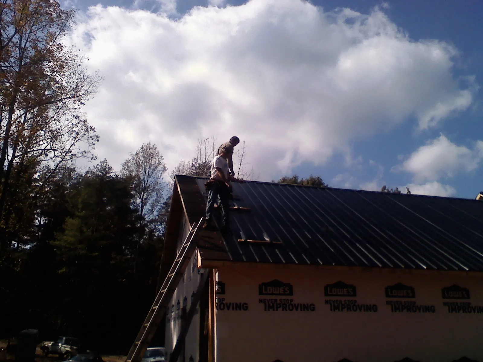 Roofer fastening dark metal panels high against a cloudy sky, from a Roof Inspection job in Floral Park