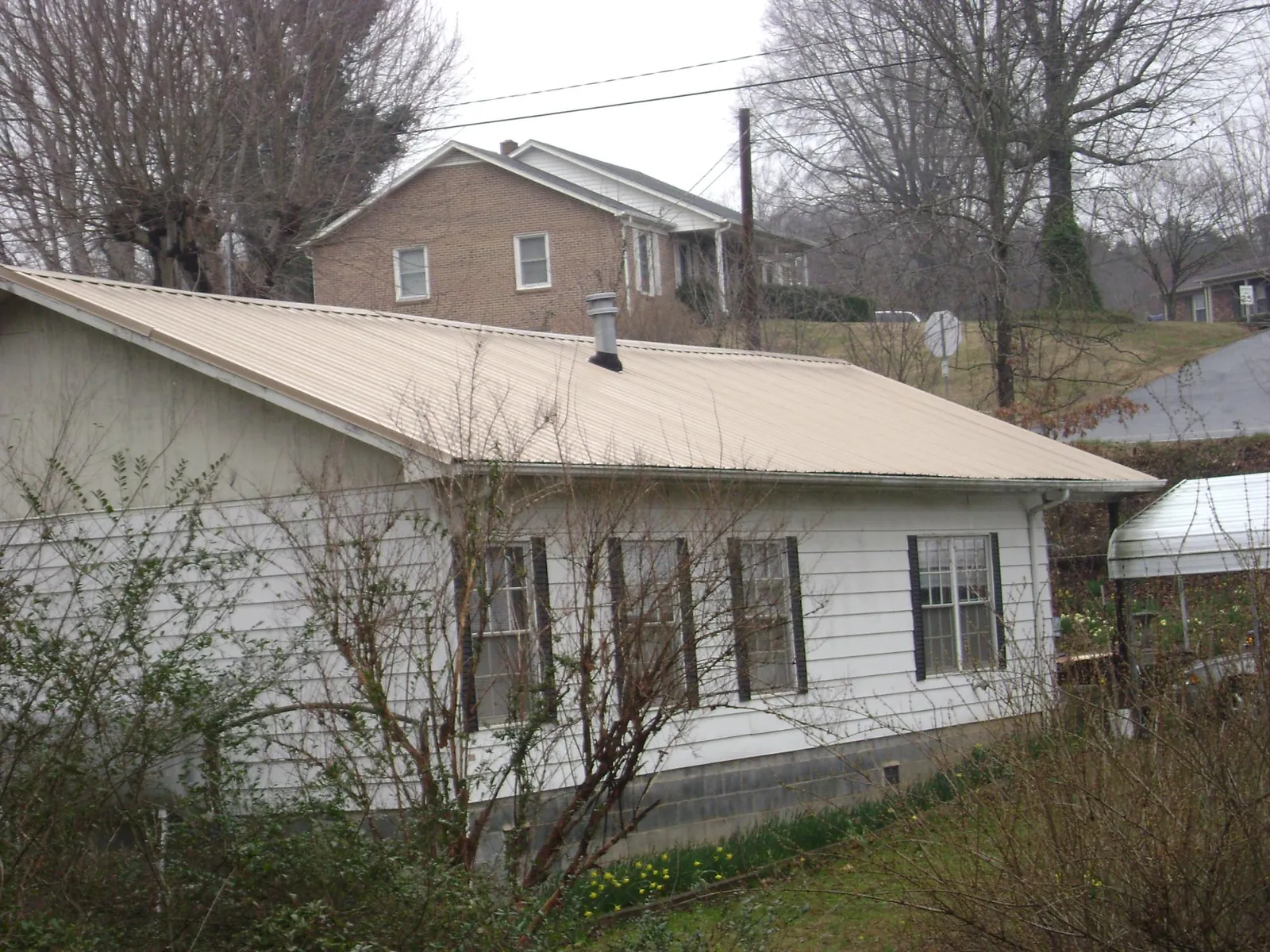 Tan metal roof on a white sided house set into a hillside — Commercial Roofing by Roofing Brothers in Floral Park