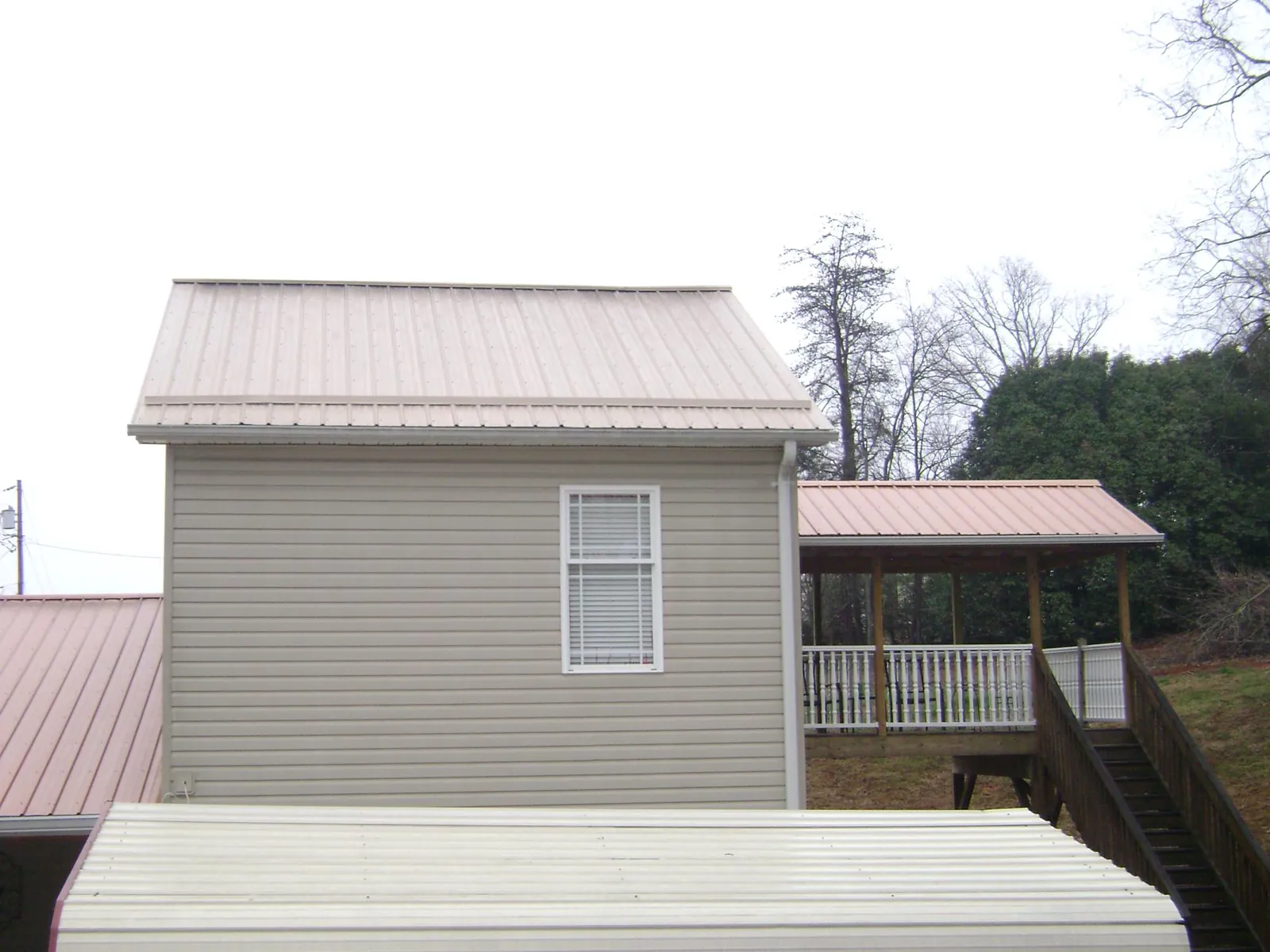 Tan metal roofs on a two story addition and attached porch, from a Roof Replacement job in Floral Park